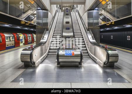 Les escaliers mécaniques d'une station de métro de Londres transportent les passagers vers le quai, représentant une scène typique des trajets urbains à Londres Banque D'Images