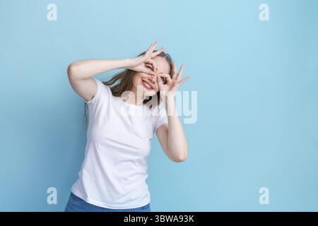 Femme drôle montrant des lunettes geste. portrait modèle féminin caucasien en blanc Banque D'Images
