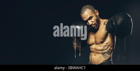 Un boxer puncher avec des gants frappe. Le combattant est Afro-américain portant des gants de boxe sur un fond sombre. Bannière publicitaire avec espace pour cop Banque D'Images
