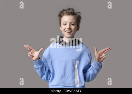 Portrait homme adolescent caucasien heureux en sweat-shirt bleu sur fond de couleur grise. Modèle masculin caucasien souriant joyeux avec un sourire blanc dans un style Banque D'Images