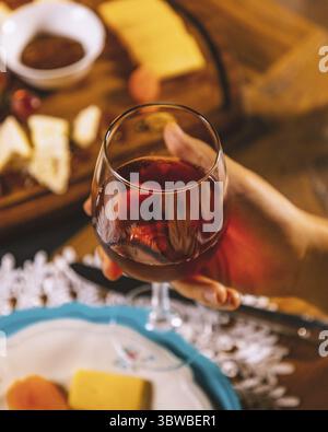Femme tenant un verre de vin rouge avec une planche à fromage avec des raisins et du miel en arrière-plan Banque D'Images