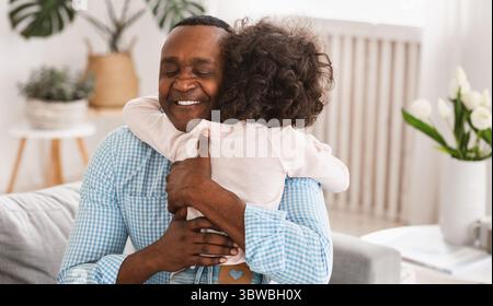 Relation grand-parent-enfant. Homme d'Afrique senior embrassant sa petite-fille à la maison Banque D'Images