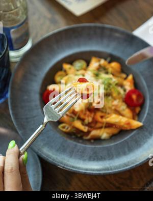 Femme tenant des pâtes penne sur la fourchette au-dessus d'une assiette de délicieux dîner de pâtes au restaurant Banque D'Images