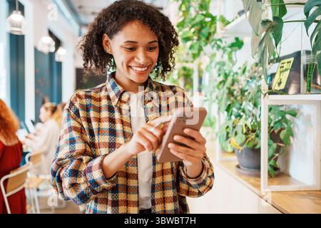 Une femme joyeuse s'engageant joyeusement avec son smartphone tout en profitant de son temps dans un café confortable Banque D'Images