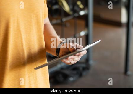 Entraîneur personnel ou culturiste tenant une tablette au gymnase ou au centre de fitness. Consultez le plan d'entraînement. Le formateur élabore un plan d'exercice. Banque D'Images