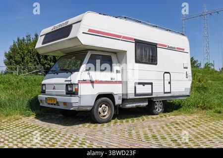 Un camping-car blanc vintage Dethleffs garé sur une zone herbeuse sous un ciel bleu vif, avec des lignes électriques en arrière-plan, faisant allusion au voyage. Nimègue, Banque D'Images