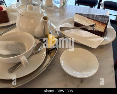 Morceau de gâteau au chocolat sur plaque blanche avec sachet de thé dans la tasse et le pot de thé, citron près de lui, dessert délicieux sucré dans le café, vue de côté en gros plan, mise au point sélective Banque D'Images