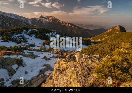 Vue aérienne du terrain accidenté, avec des sommets poussiéreux de neige et des affleurements rocheux captant la lumière dorée du soleil couchant, Zakopane, Województwo Małopolskie, Pologne. Banque D'Images