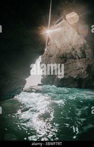 Une grotte avec un trou dedans et un jet d'eau en sort. L'eau est claire et le soleil brille à travers le trou Banque D'Images