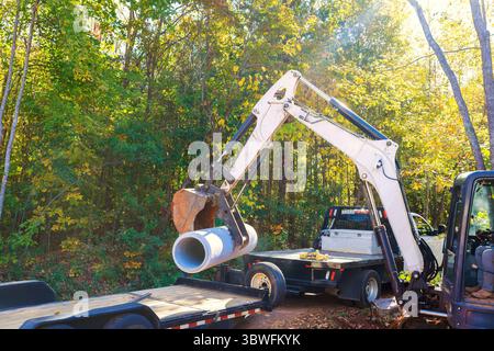 La pelle lourde manipule un gros tuyau de ciment de drainage sur une remorque de construction au milieu du chantier Banque D'Images