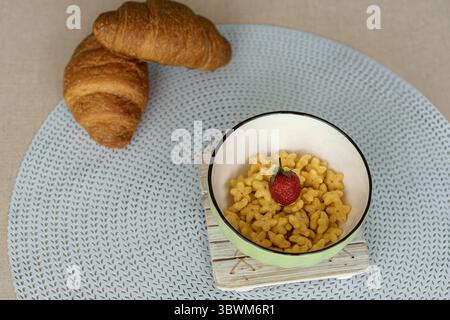 Concept de petit déjeuner sain. Un bol vert de céréales en forme d'étoile surmonté d'une fraise fraîche, avec des croissants sur un napperon bleu. Banque D'Images