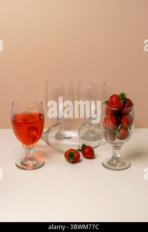 Nature morte créative avec verrerie. Un verre de boisson à la fraise, un autre rempli de fraises fraîches et des verres vides sur une table. Banque D'Images