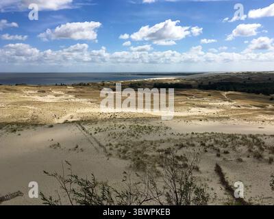 Vastes dunes de sable près de Neringa, Lituanie, dans le parc national de Curonian Spit, avec une végétation clairsemée et la mer Baltique sous un ciel partiellement nuageux. Banque D'Images