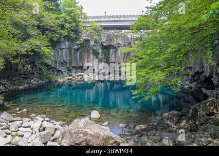 Eau turquoise limpide entourée de falaises basaltiques colonnaires et de verdure luxuriante à la piscine de Cheonjeyeon Falls, île de Jeju, Corée du Sud. Banque D'Images