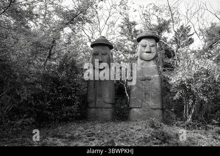 Deux statues traditionnelles de Dol Hareubang en noir et blanc, situées dans une forêt sur l'île de Jeju, Corée du Sud. Banque D'Images
