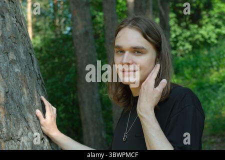 Un jeune individu se tient doucement près d'un grand arbre, profitant de l'environnement serein de la forêt. Banque D'Images