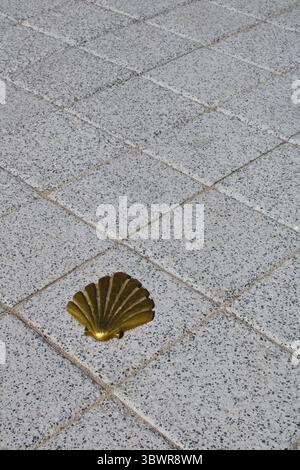 Coquille de Saint-Jacques dorée encastrée dans un trottoir de granit marquant la voie pour les pèlerins marchant sur le Camino de santiago Banque D'Images