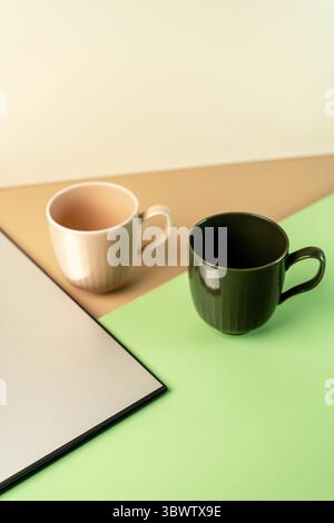 Deux mugs vides en céramique côtelée, vert foncé et beige, disposés sur un fond géométrique moderne de vert, beige et gris. Concept de vaisselle élégant. Banque D'Images