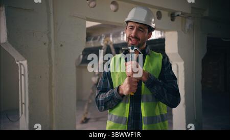 Joyeux homme caucasien actif constructeur tenant l'outil de travail de marteau utilisant comme microphone chantant chanson positive profiter de la musique homme Guy architecte entrepreneur Banque D'Images