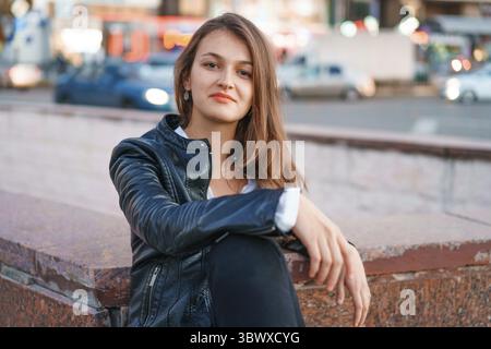 Portrait jeune belle femme rousse à la mode avec des taches de rousseur, de longs cheveux bouclés, dans des vêtements de jeunesse décontractés, posant sur une rue de la ville. Avec un triste expres Banque D'Images