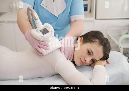 Belle femme brunette obtenant la thérapie cosmétique anti-cellulite avec machine GPL. Femme masseuse fait un massage GPL des cuisses. Massage corporel raffermissant au GPL Banque D'Images