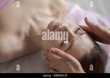 Cosmétologue ou massothérapeute faisant la main relaxant rajeunissant visage et épaule massage pour jeune femme dans le salon de beauté, vue arrière. Rajeunissant Banque D'Images
