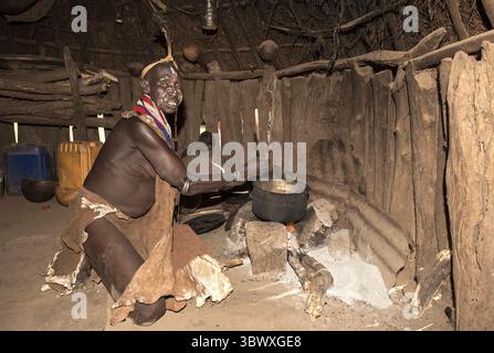 Femme Nyangatom préparant une bouillie de sorgho sur un feu de bois dans sa cabane, groupe ethnique du Nyangatom, également connu sous le nom de Bume, South Omo Valley, Ethiopie Banque D'Images