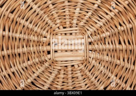 Vue rapprochée d'un panier rond en osier avec un motif d'armure complexe. La texture naturelle met en valeur l'artisanat avec des tons chauds, mis sur un fond Uni pour l'accent. Banque D'Images