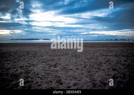 Coucher de soleil sur les vastes plages d’Essaouira avec un ciel bleu, des nuages blancs et des vagues s’écrasant sur le rivage au Maroc Banque D'Images