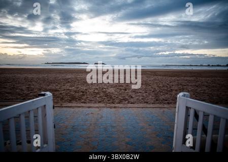 Coucher de soleil sur les vastes plages d’Essaouira avec un ciel bleu, des nuages blancs et des vagues s’écrasant sur le rivage au Maroc Banque D'Images
