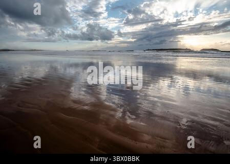 Coucher de soleil sur les vastes plages d’Essaouira avec un ciel bleu, des nuages blancs et des vagues s’écrasant sur le rivage au Maroc Banque D'Images