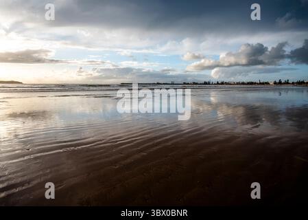 Coucher de soleil sur les vastes plages d’Essaouira avec un ciel bleu, des nuages blancs et des vagues s’écrasant sur le rivage au Maroc Banque D'Images