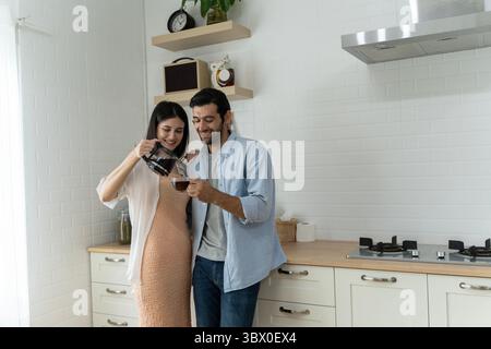 Jeune couple partageant Happy Morning café Time dans leur cuisine moderne. Femme verse amoureusement le café chaud pour l'homme souriant tout en se tenant debout ensemble, créat Banque D'Images