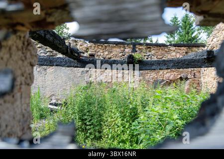 Vue à travers une ouverture carbonisée d'un ancien bâtiment en pierre en ruine avec des mauvaises herbes envahies et une forêt en arrière-plan. Banque D'Images