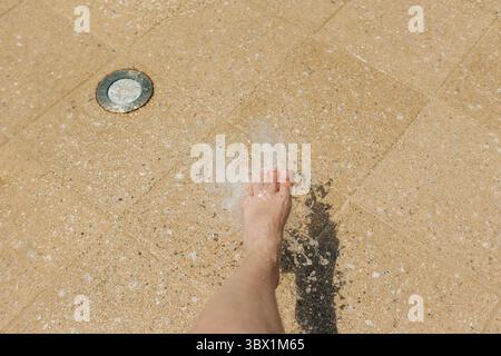 Un pied entre dans les éclaboussures d'eau, profitant de la fraîcheur par une journée brillante dans un espace de jeux d'eau. Banque D'Images