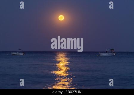 Une lune brille sur l'eau et le ciel est sombre. Il y a deux bateaux dans l'eau en Grèce Banque D'Images