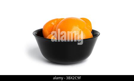 Pêches en conserve dans un bol noir. Pêches douces au sirop isolé sur fond blanc. Photo de haute qualité Banque D'Images