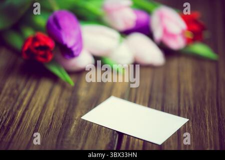 Rendu 3D montrant une carte rectangulaire blanche vierge sur une table en bois avec bouquet de tulipes floues. Rustique, élégant, floral, minimaliste, naturel, guerre Banque D'Images
