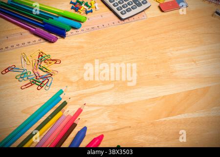 Grappe de crayons de couleur, trombones, stylos et règle repose sur la gauche du bureau en bois clair. Fournitures de bureau, papeterie, organisation, créativité, Banque D'Images