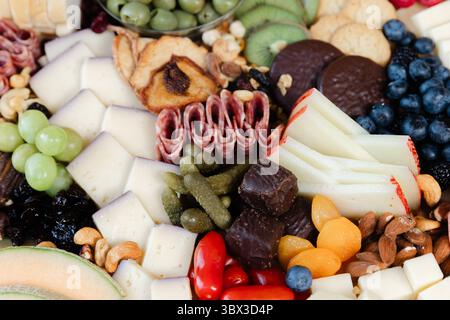 Une gamme vibrante de fromages, viandes, fruits et noix disposés magnifiquement sur une planche de bois pour une réunion invitante. Banque D'Images