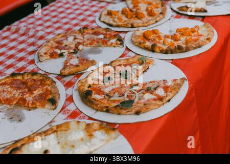 Un assortiment coloré de pizzas disposées sur une nappe à carreaux rouge lors d'un festival culinaire animé. Banque D'Images