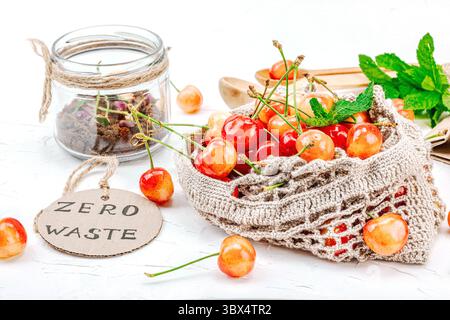 Cerises mûres douces dans un sac de coton sur une planche de bois rustique, à côté d'un pot de compost avec des fleurs séchées et une étiquette zéro déchet, favorisant une vie durable Banque D'Images