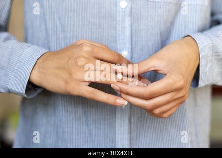 Gros plan sur la bague de fiançailles d'une femme. Gros plan d'une main de femme plaçant une bague de fiançailles en diamant sur son doigt tout en portant une chemise rayée Banque D'Images