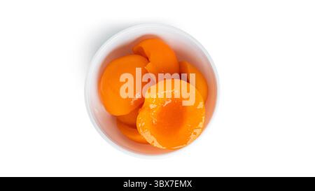 Pêches en conserve dans un bol blanc. Pêches douces au sirop isolé sur fond blanc. Photo de haute qualité Banque D'Images