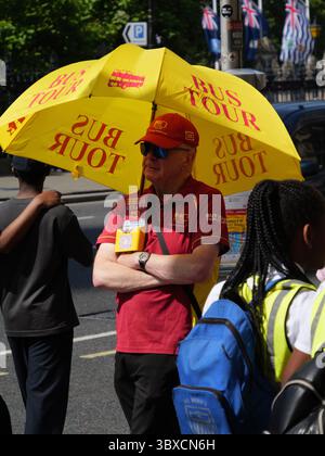 Un vendeur Big bus Tours se tient devant la gare de Westminster, se protégeant du soleil d'été avec un parapluie, tandis que les touristes explorent l'un des endroits les plus emblématiques de Londres près du Parlement et de Big Ben Banque D'Images