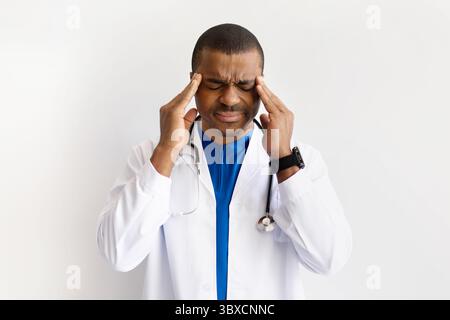 Médecin noir stressé touchant les tempes, souffrant de maux de tête, yeux fermés dans la douleur Banque D'Images
