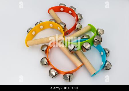 Une collection de petits tambourins en cloche jingle vibrante de différentes couleurs avec des poignées en bois, disposés sur une surface blanche, prêts à faire de la musique. Banque D'Images