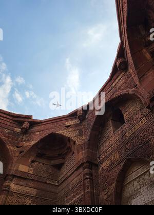 Arches mogholes historiques à Qutub Minar, Delhi, avec avion traversant le ciel. Banque D'Images