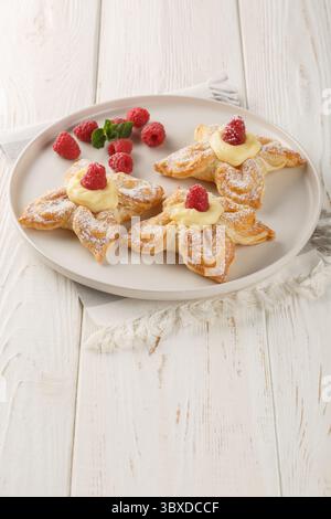 Gâteau en forme de fleur feuilletée avec crème anglaise et framboises fraîches gros plan dans une assiette sur la table. Vertical Banque D'Images