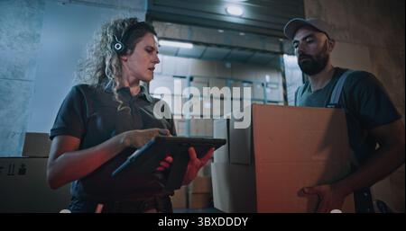 Gestionnaire d'inventaire féminin scannant des boîtes de carton avec scanner de code à barres, en utilisant un ordinateur tablette. Travailleurs multiethniques transportant des colis avec des commandes en ligne, marchandises de Logistics Retail Warehouse la nuit. Banque D'Images